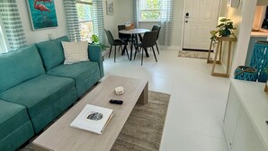 Un salon moderne avec un canapé de couleur turquoise, une table basse en bois et un coin repas comprenant une table et des chaises.