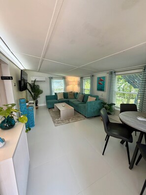 A modern living room with a sectional sofa, a coffee table, and a dining area with a table and chairs. - Shady Acres Owner’s Suite (Stuart)