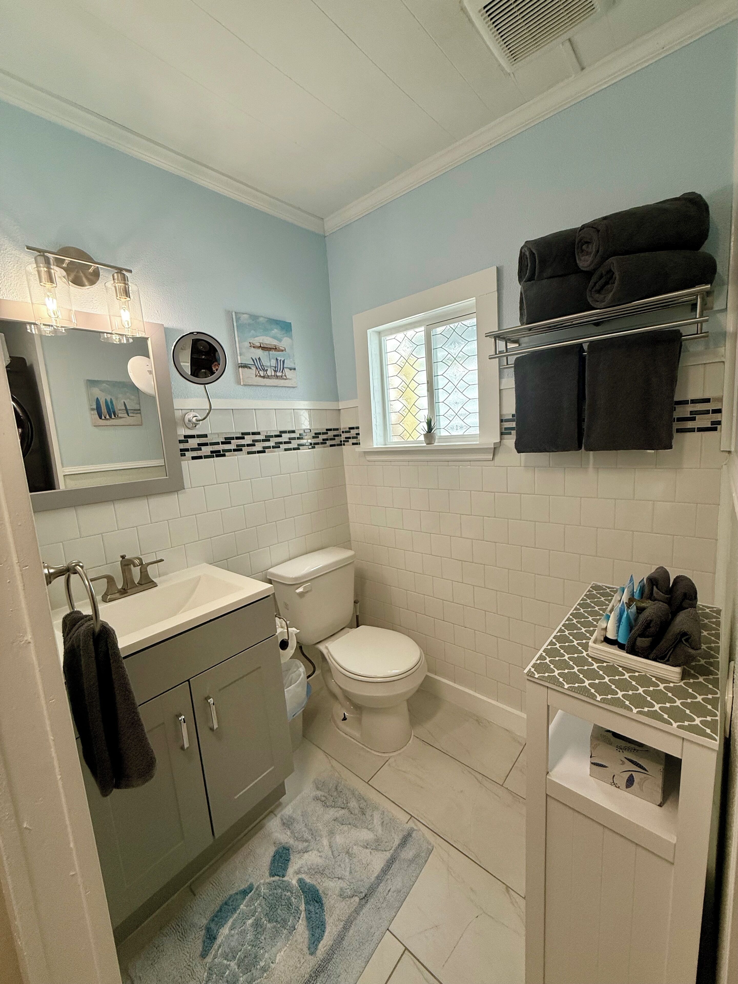 Een badkamer met toilet, wastafel, spiegel, handdoekrek en een raam.