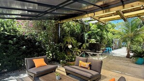 Une terrasse extérieure dotée d’un espace salon abrité, d’un sol en pierre et d’une végétation luxuriante.