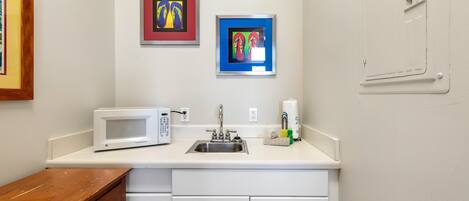 Una cocina con armarios blancos, un microondas, un fregadero y dos obras de arte enmarcadas en la pared.