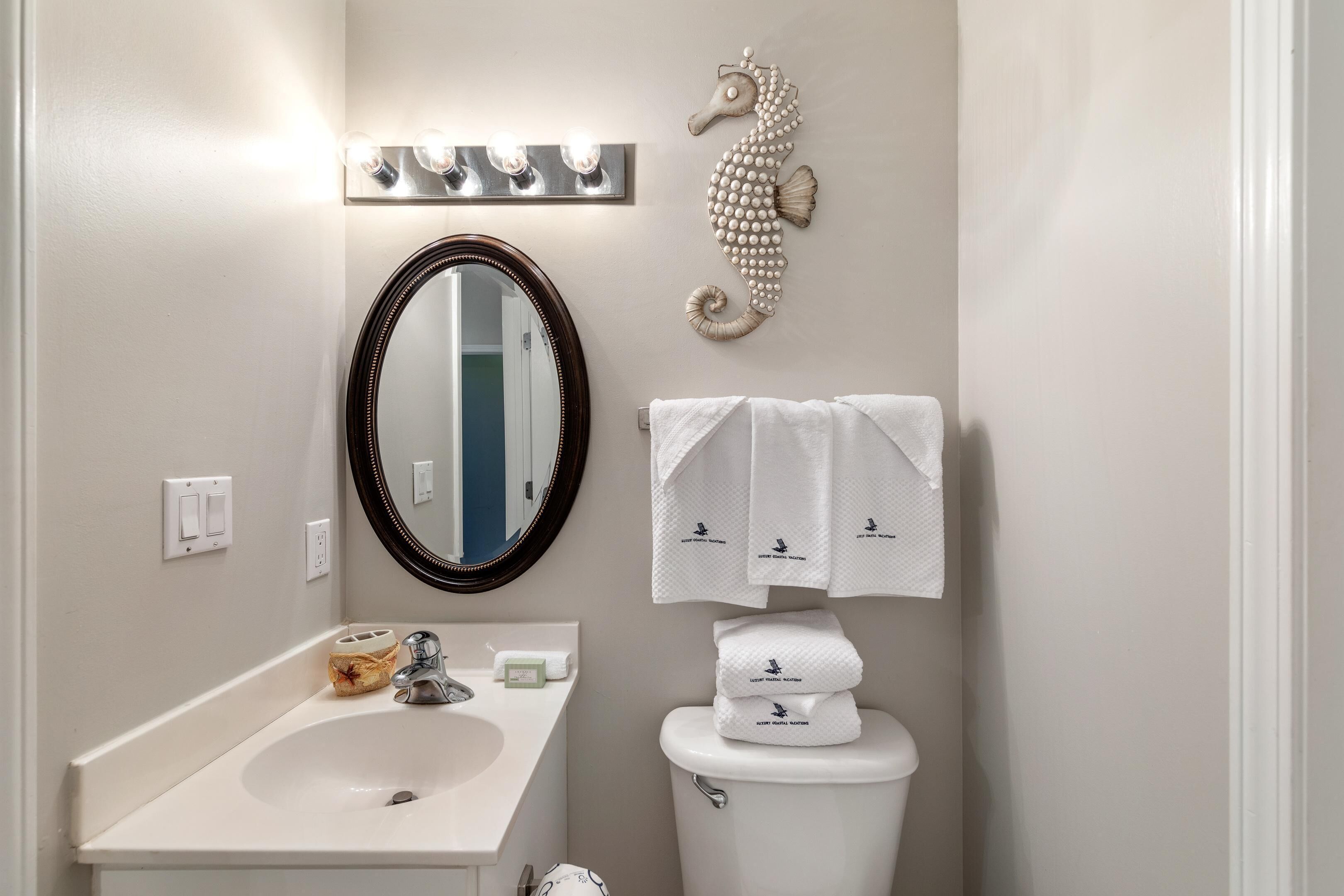 Une salle de bain avec un lavabo blanc, un miroir, des toilettes et des serviettes décoratives.