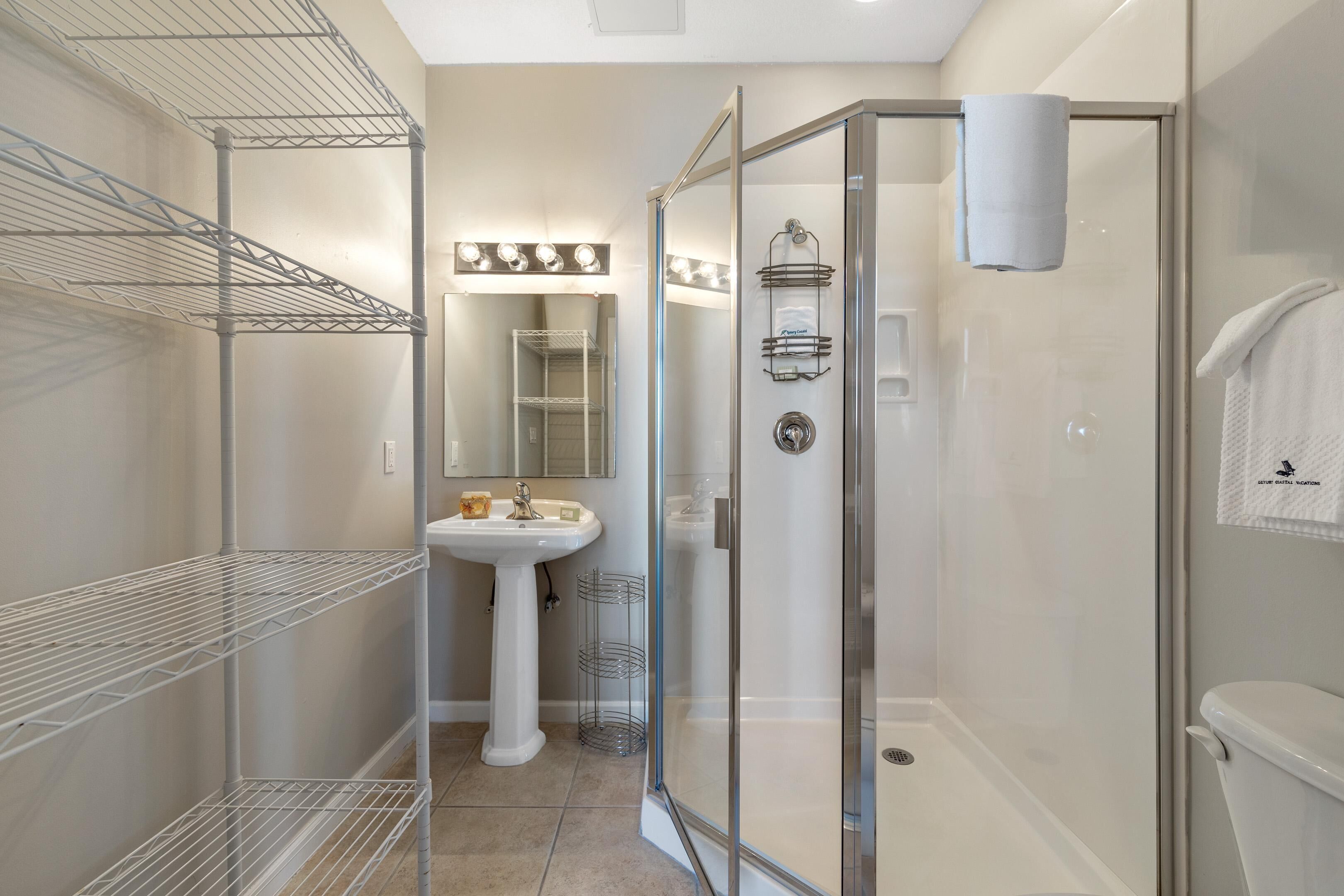 A bathroom with a glass-enclosed shower, a white sink, and metal shelves.