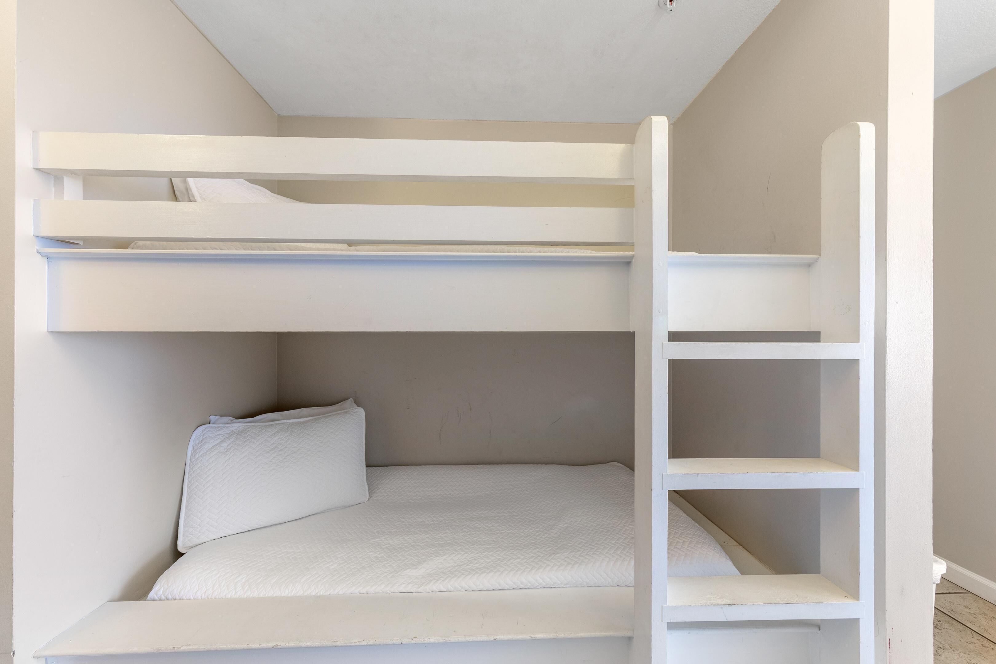 A bunk bed with a ladder, a pillow, and a white wall.