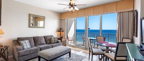 A hotel room with a balcony, a sofa, a dining table, and a TV.