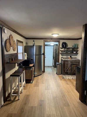 Kitchen area with central island, refrigerator, and sink, featuring a door to another room and basic amenities.