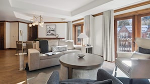 Un salon moderne avec une table basse ronde, un canapé et un fauteuil. On y trouve également un coin repas avec une table et des chaises, et une vue sur un immeuble à travers de grandes fenêtres.