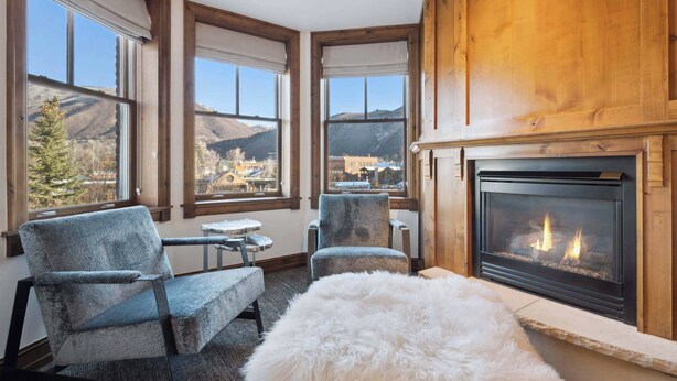 Una habitación acogedora con chimenea, ventanas amplias con vistas a la montaña y asientos cómodos.