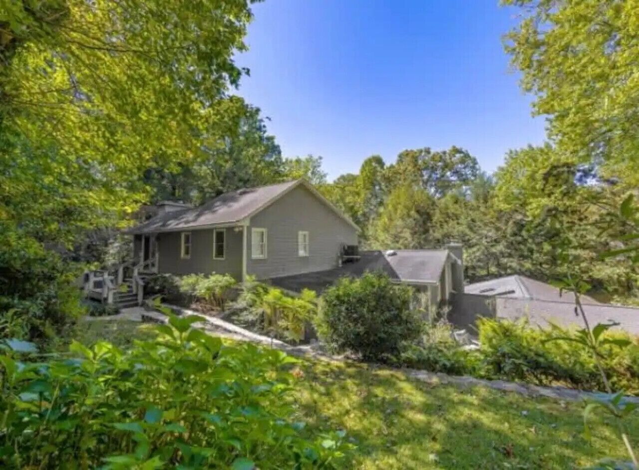 A single-story house with a sloped roof, surrounded by dense greenery and trees.