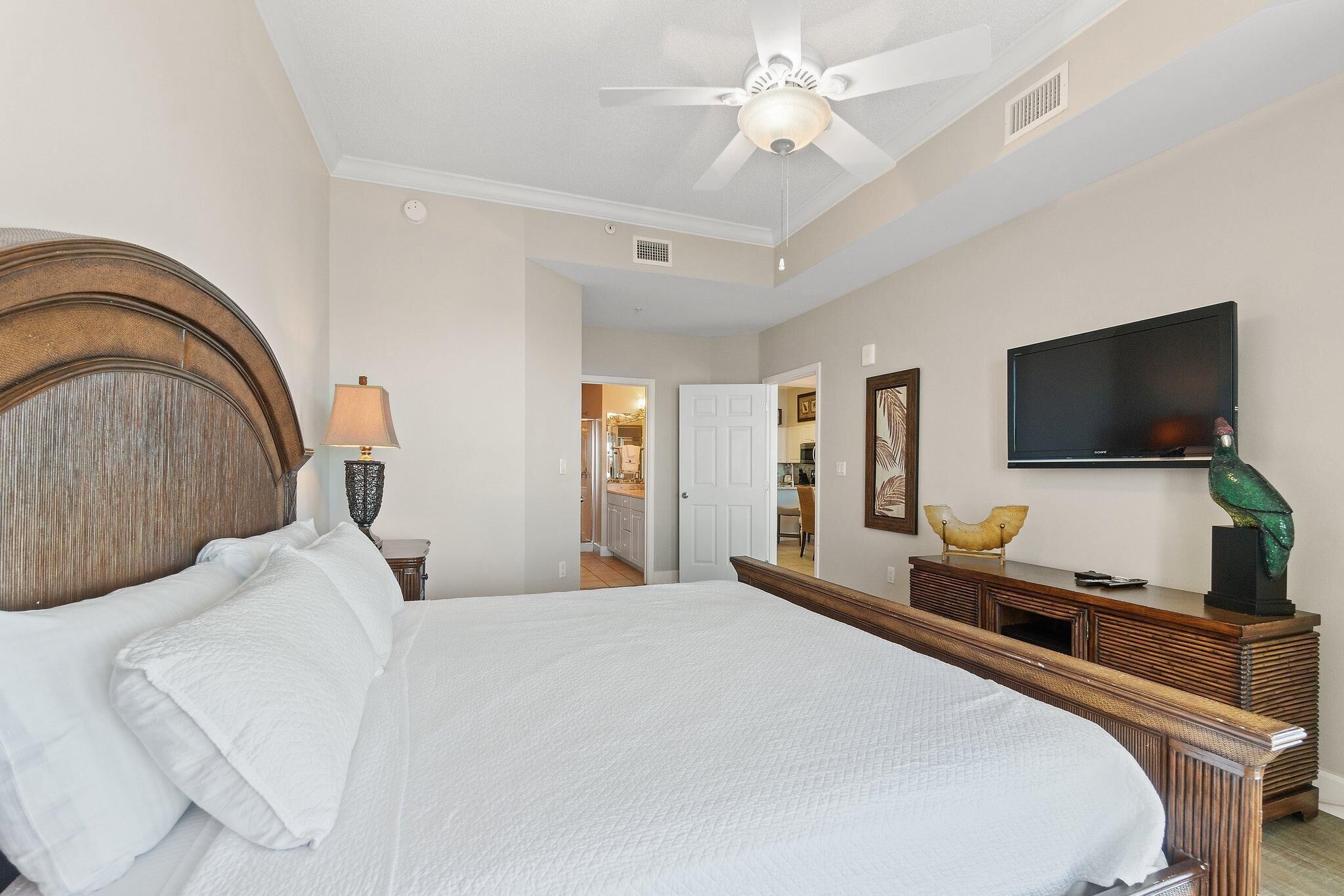 A bedroom with a large bed, a ceiling fan, a TV, and a wooden dresser.