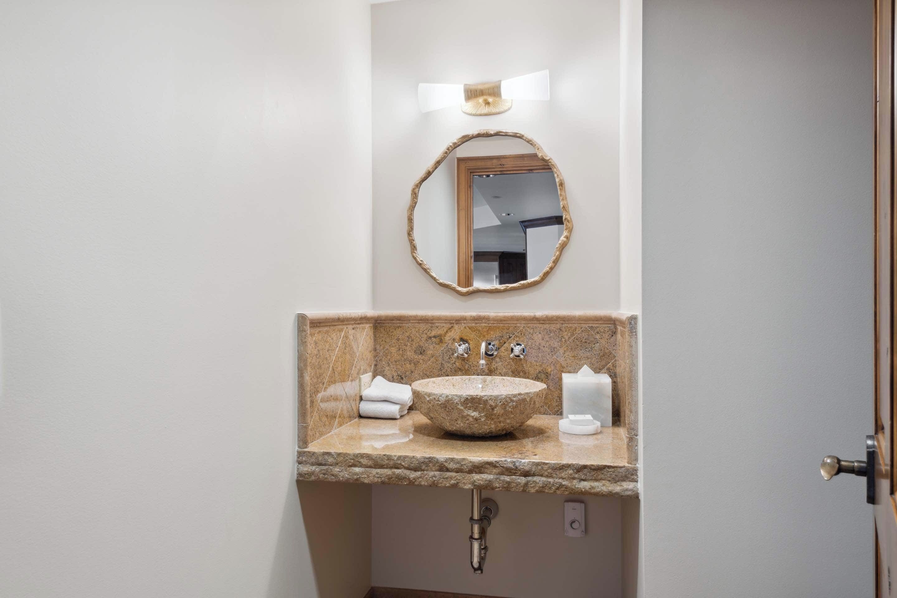 A bathroom with a stone sink, two faucets, a mirror with a wooden frame, and a towel on the counter.