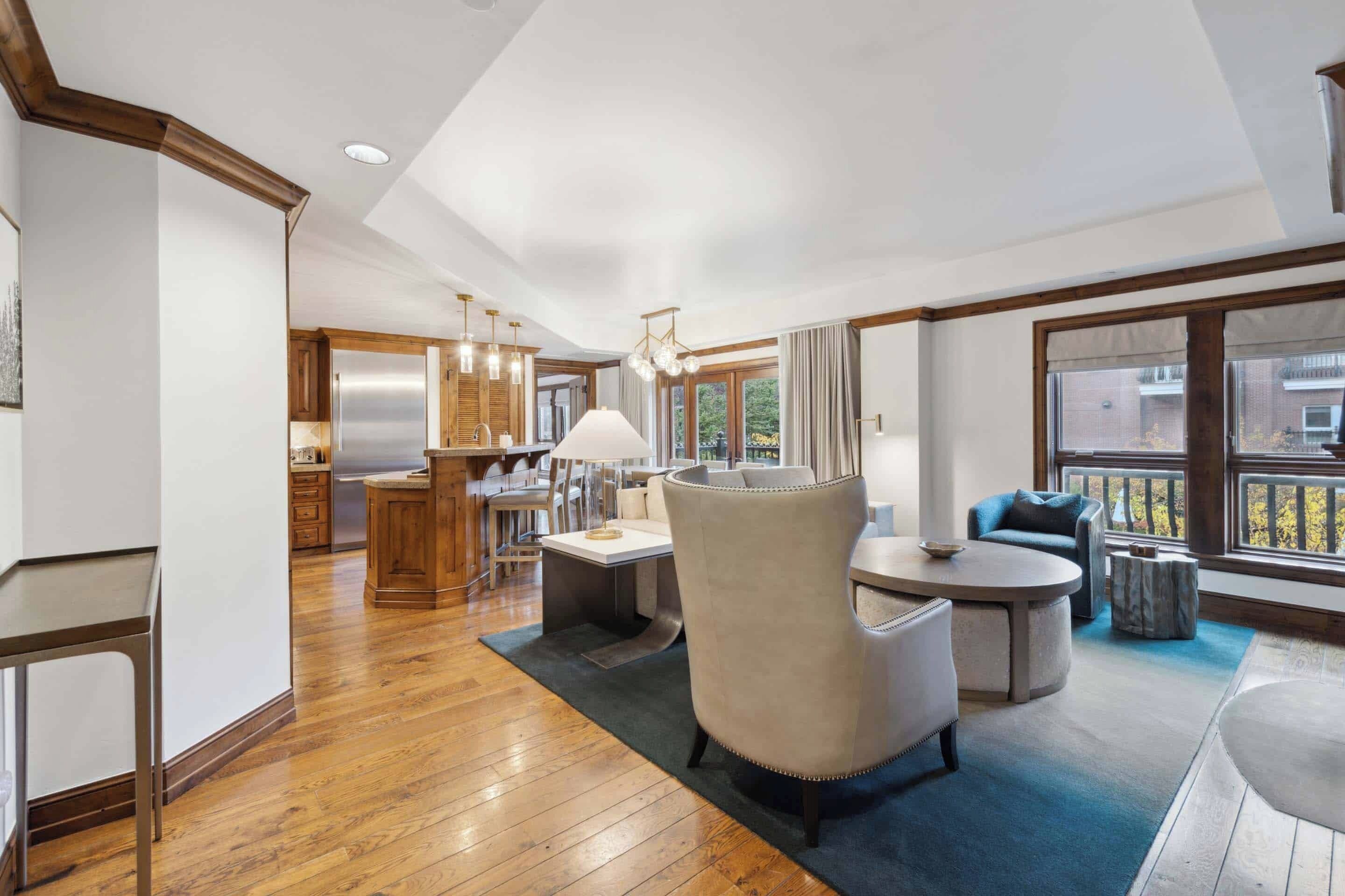 A modern kitchen with wooden cabinets and stainless steel appliances, a dining area with a round table and chairs, and large windows offering views of the outside.