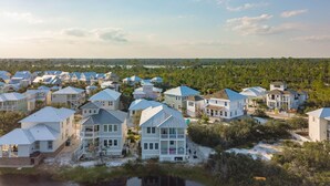 Un quartier résidentiel situé sur la côte, avec des maisons dotées de toits à pignons et de balcons, entouré d’une végétation luxuriante et bordé par une étendue d’eau en arrière-plan.