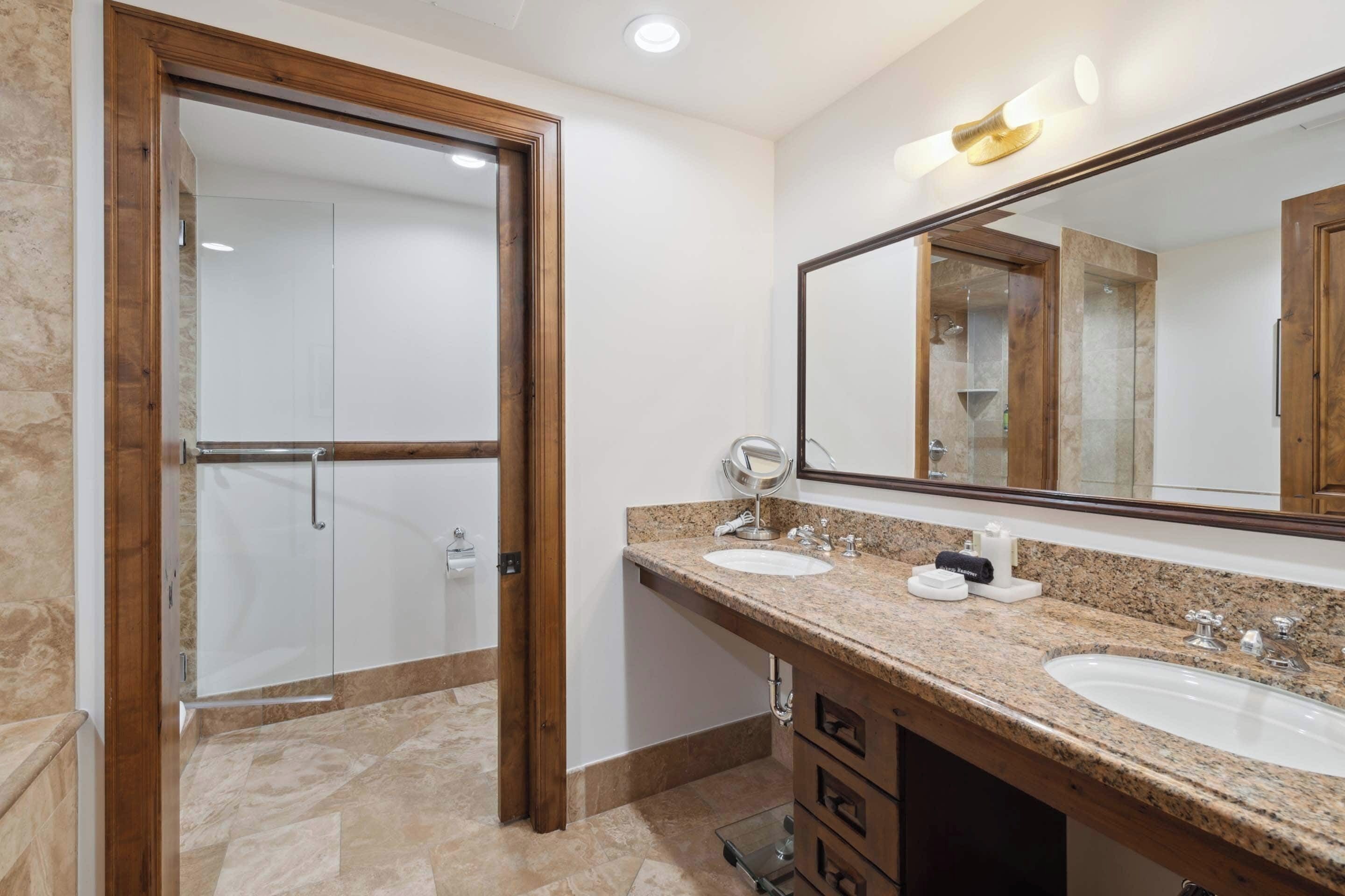 A bathroom with two sinks, a large mirror, and a shower area.