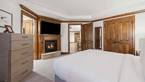 Un dormitorio con una cama grande, chimenea, puertas de madera y televisor.
