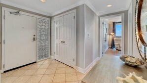 A hallway with a white door, a glass door with a floral pattern, and a wooden bench with decorative shells. - Phoenix Viii 1506 (Orange Beach)