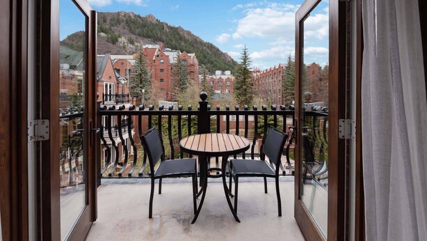 Ein Balkon mit Tisch und Stühlen, der Blick auf Gebäude und einen Berg gewährt.