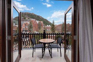 Un balcon avec une table et des chaises, d’où l’on peut admirer des bâtiments et une montagne.