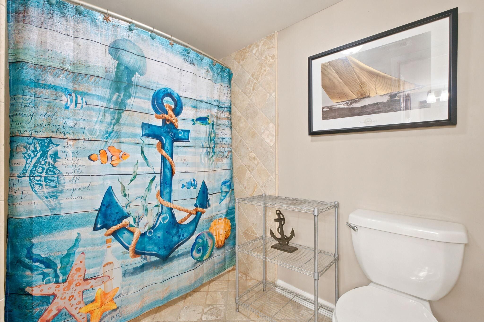 Un bagno con un murale a tema nautico, un quadro incorniciato sopra il water e un mobiletto a giorno accanto al wc.
