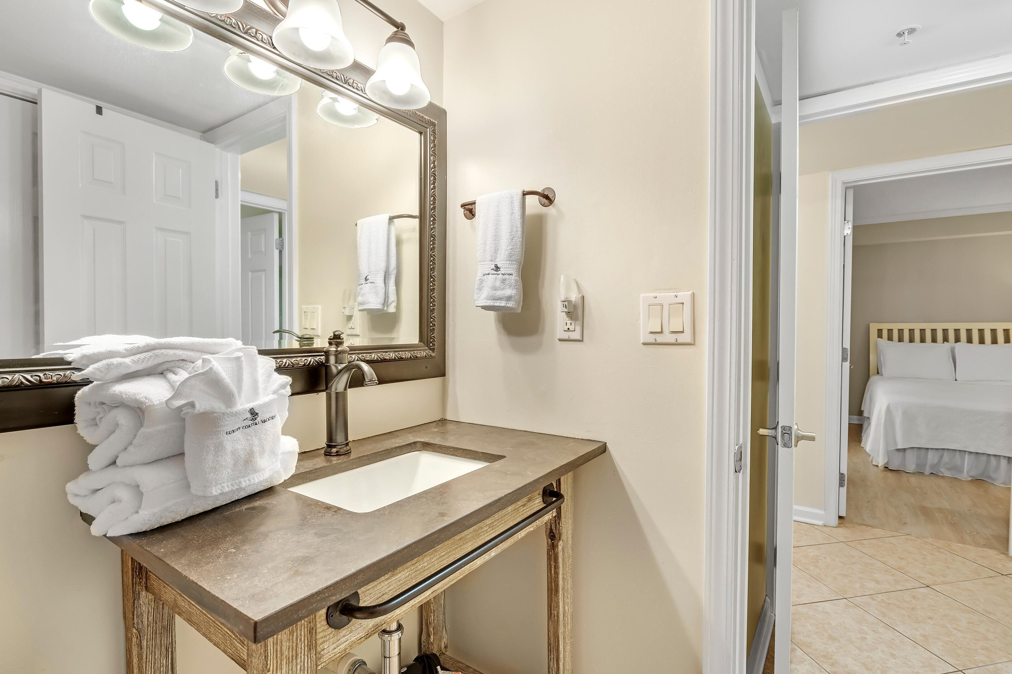 A bathroom with a sink, mirror, towel rack, and a door leading to a bedroom.