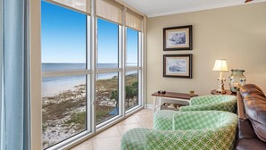 A room with a large window offering a view of the beach, a ceiling fan, and a small table with a lamp. - Seaspray West 503- Gulf Front (Pensacola)
