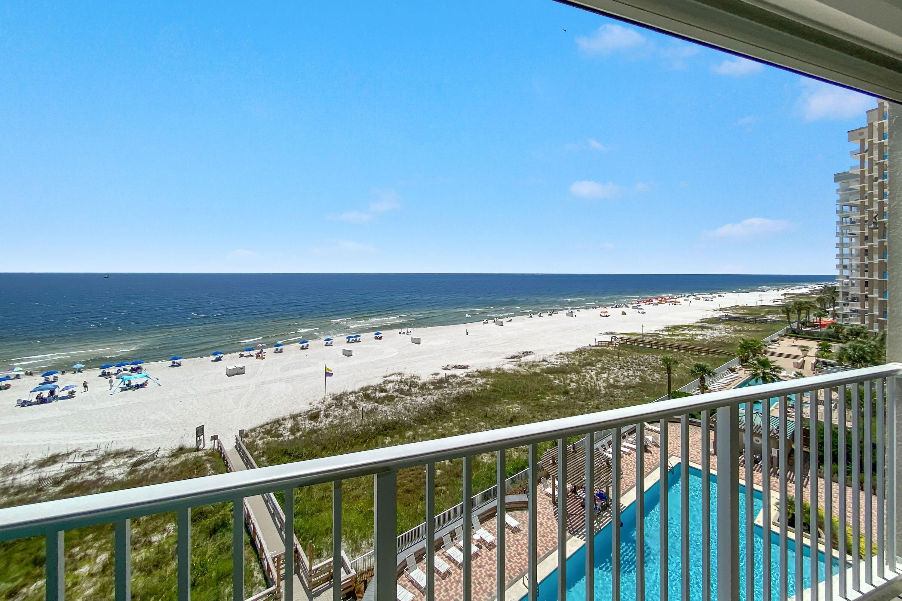 A view from a balcony overlooking a beach with a pool and a clear sky.