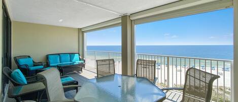 A balcony with a glass table and chairs, a sofa, and a view of the ocean.