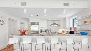 A modern kitchen with white cabinetry, stainless steel appliances, and a central island with bar stools. - Vista Del Mar 201 (Pensacola)