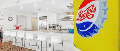 A modern kitchen with white cabinetry, a bar area with white stools, and a large Pepsi logo on a yellow door.
