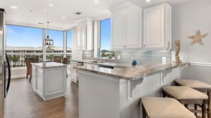 A spacious kitchen with white cabinetry, a large island, and a view of a residential area. - La Playa 301 (Pensacola)