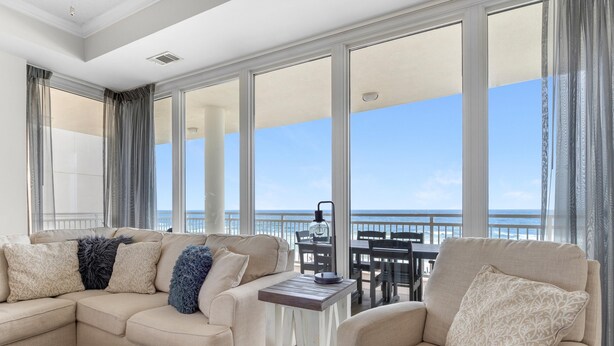 A balcony with a beige sofa, a small table, and a view of the ocean. - La Playa 301 (Pensacola)
