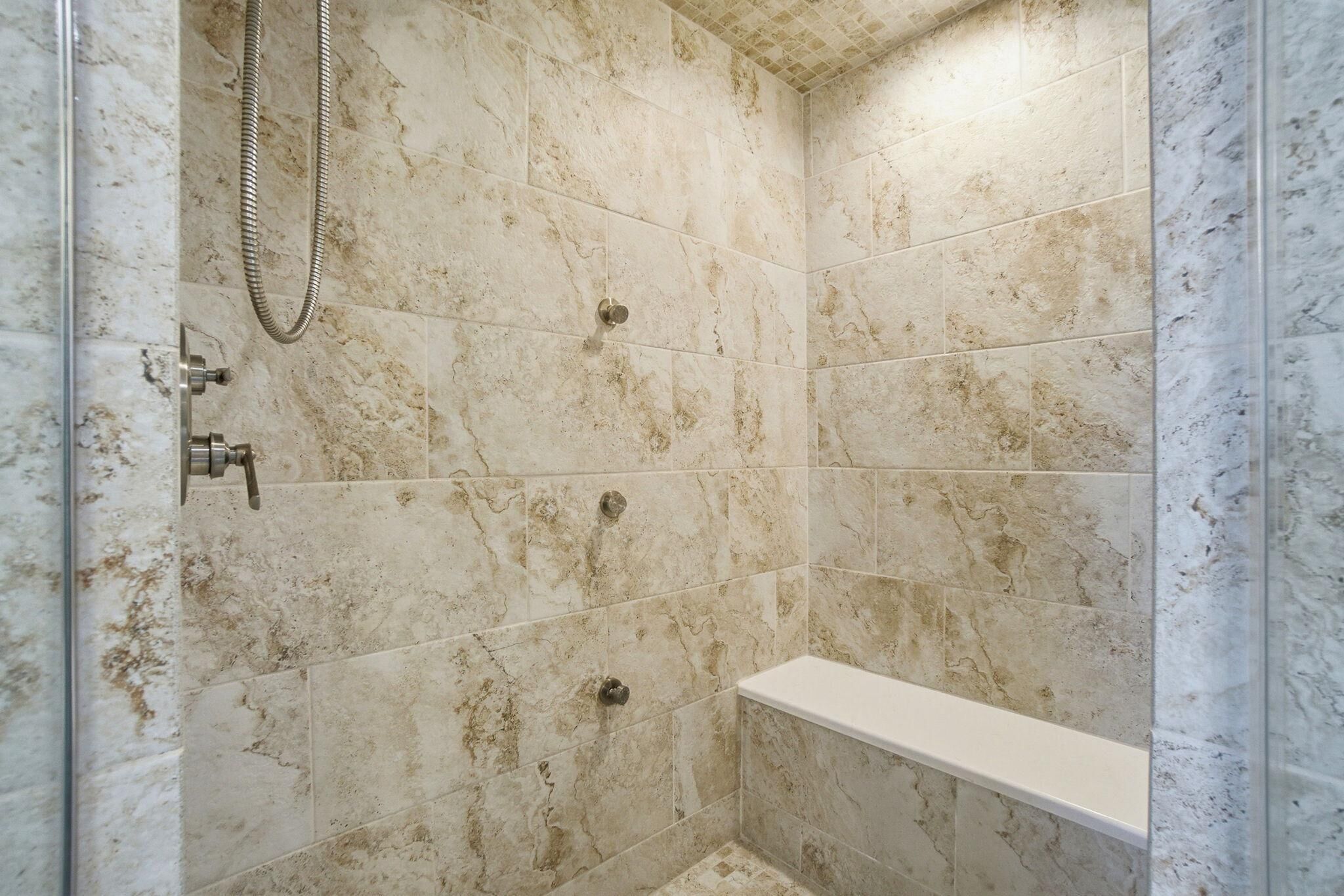 A bathroom with marble tiles, a showerhead, and a white bench.