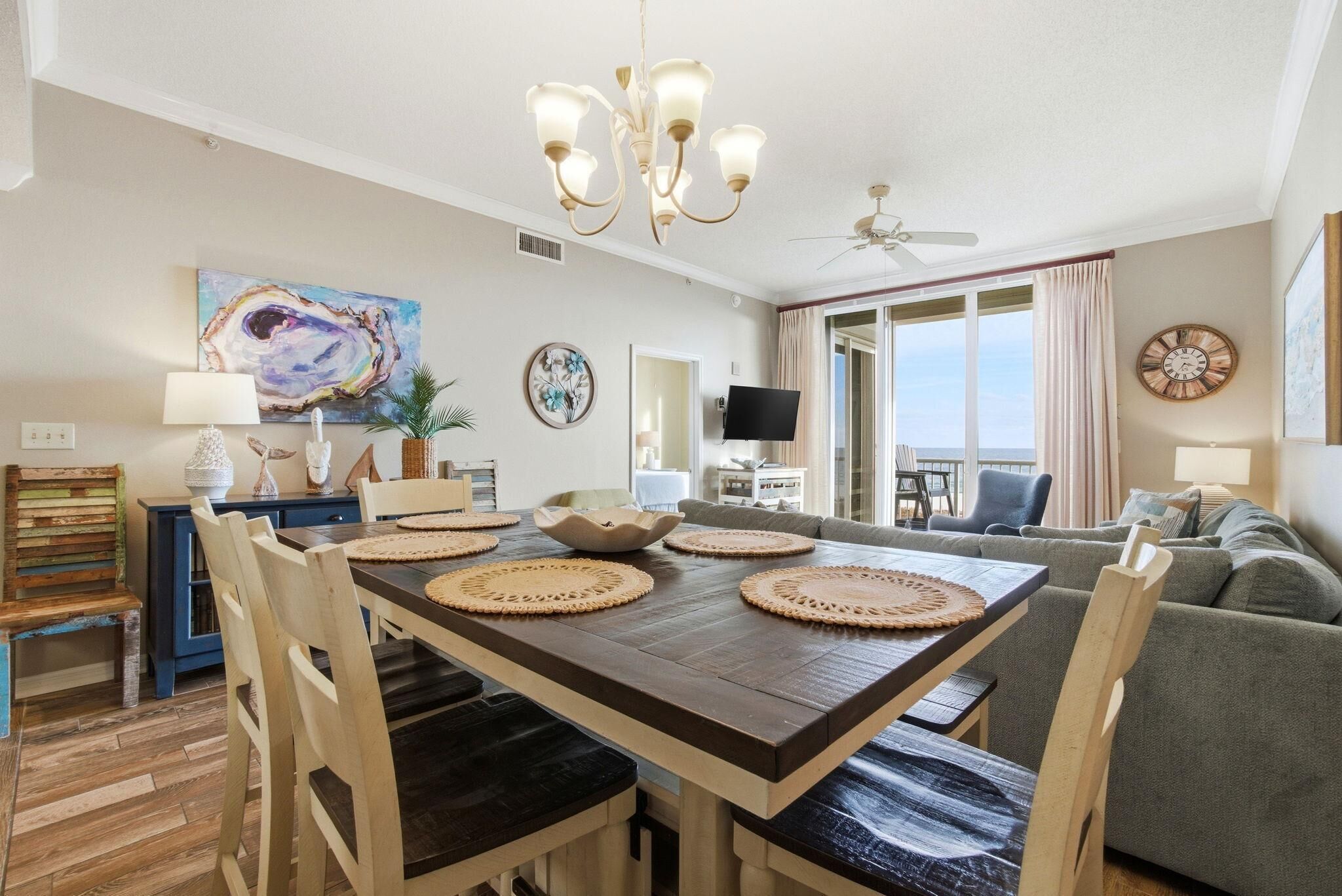 A dining area with a wooden table, four chairs, a chandelier, and a television in the background.