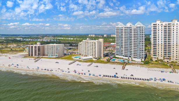 A beachfront hotel with multiple high-rise buildings, a sandy beach, and a clear sky. - Perdido Sun 712 (Pensacola)
