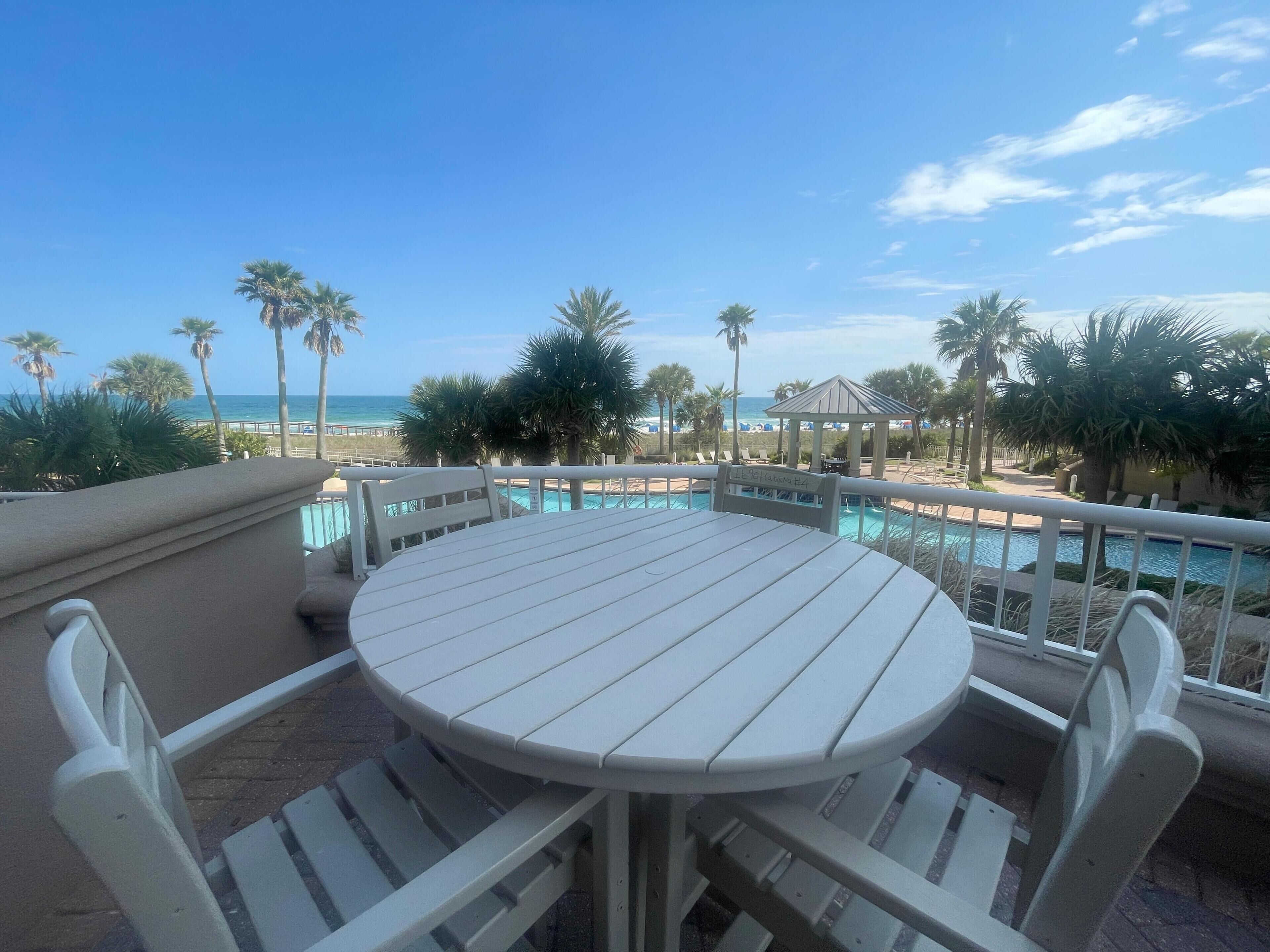 A round table with chairs, a pool, and a beach view.