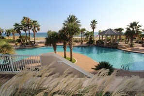 Un espace piscine agrémenté de palmiers, de chaises longues et d’un belvédère offrant une vue sur la plage.