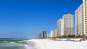 A beach with high-rise buildings, clear skies, and ocean waves.