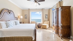 A bedroom with a large bed, a wardrobe, a chair, and a view of the ocean. - Indigo East 1602 (Pensacola)