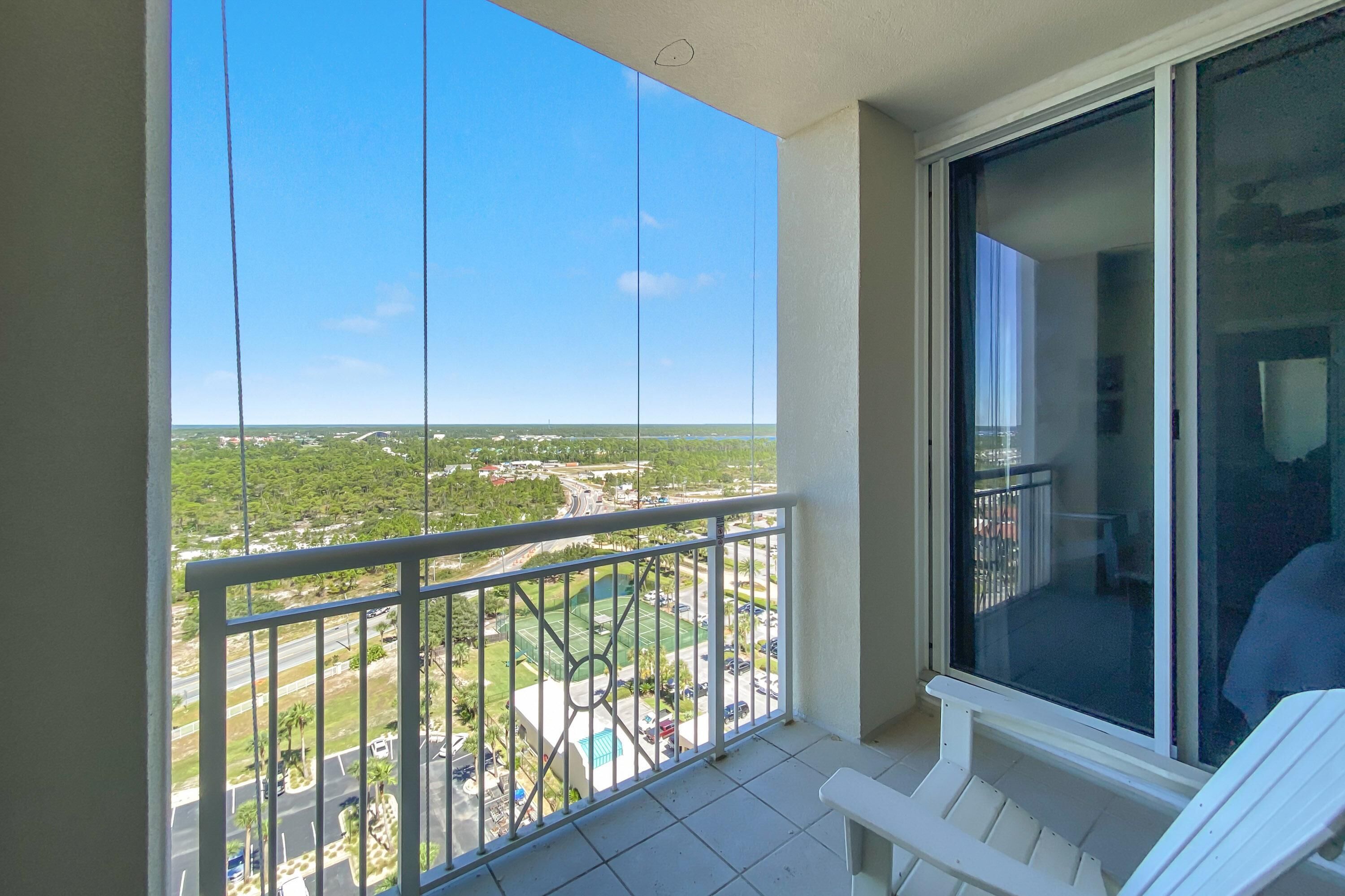 A balcony with a clear view of a green landscape and a parking area.