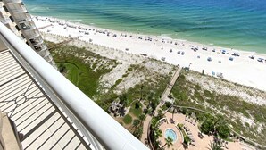 A beach view from a balcony with a pool area, beach umbrellas, and lounge chairs. - Indigo East 1602 (Pensacola)