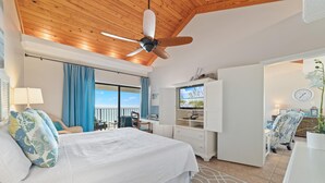 A bedroom with a large bed, a ceiling fan, a TV, and a view of the ocean. - Shipwatch A804 (Pensacola)