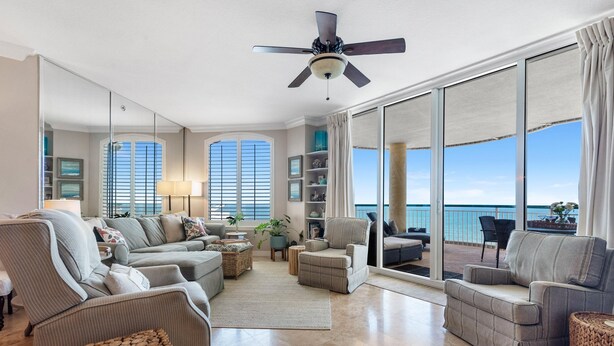 A spacious living room with a large window, a ceiling fan, and a view of the ocean. - Beach Colony East 16b-penthouse (Pensacola)