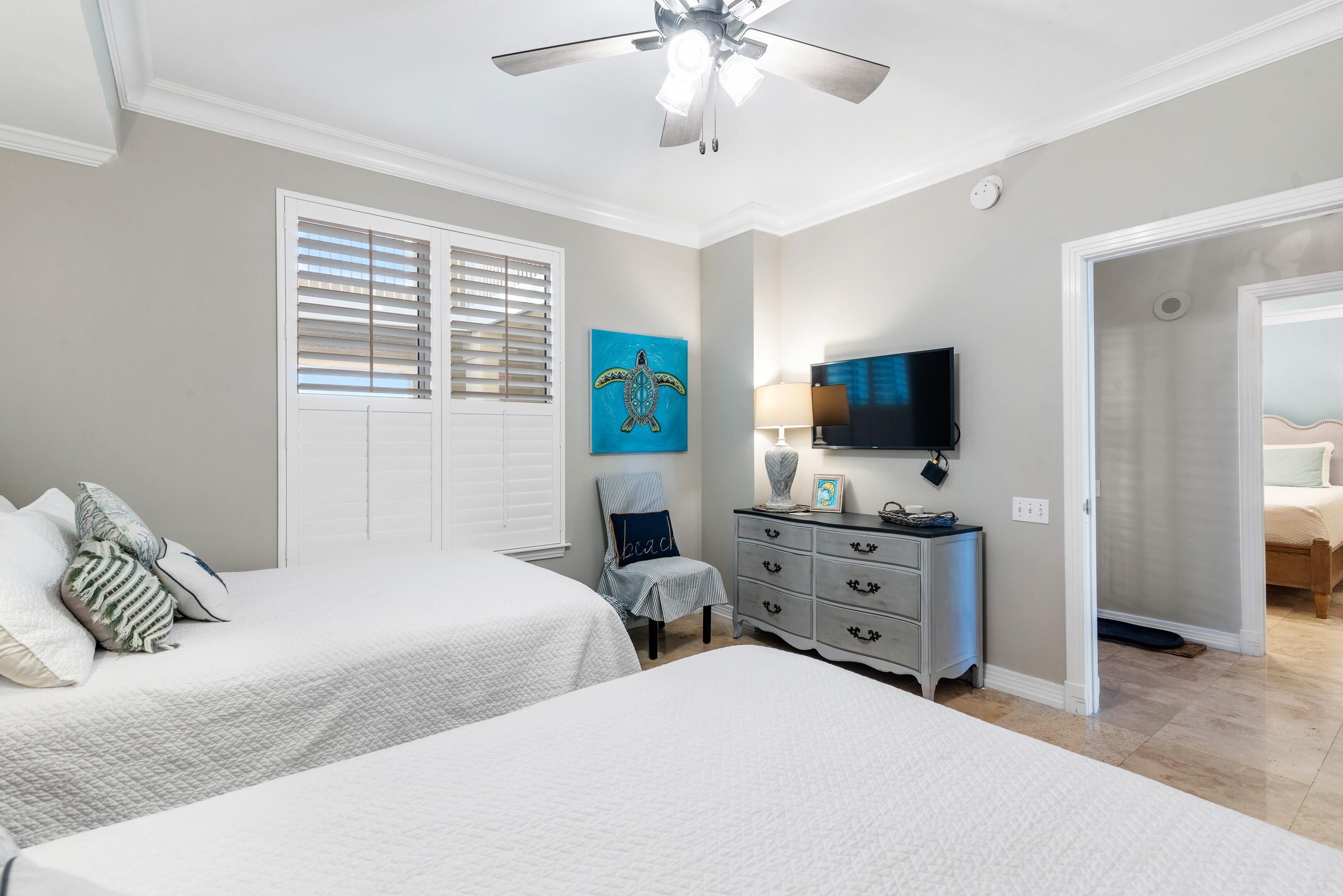 A bedroom with two beds, a ceiling fan, a television, and a painting of a turtle.