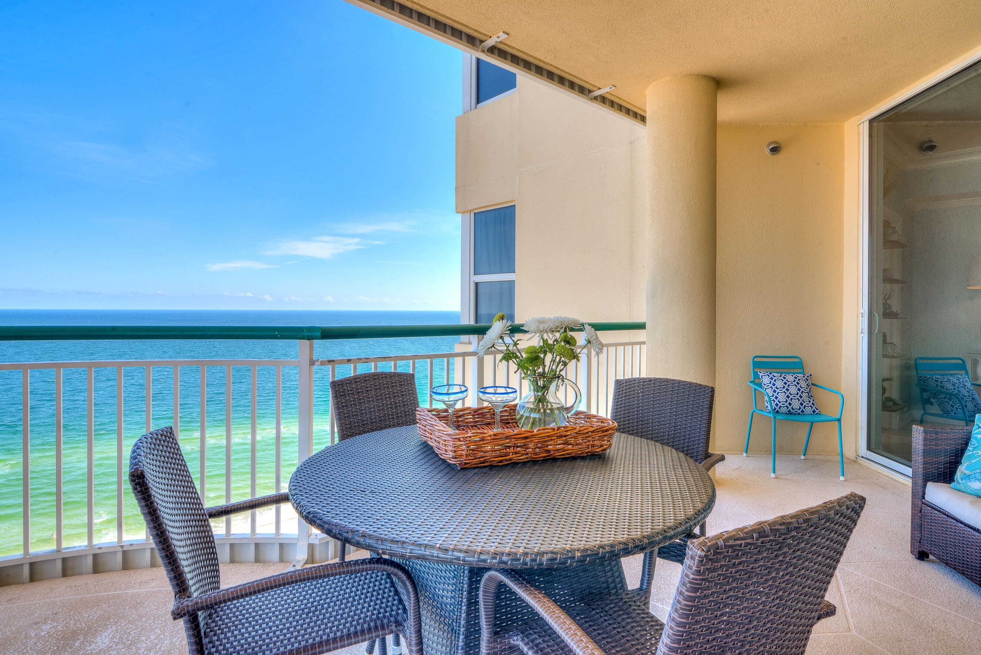 A balcony with a round table, wicker chairs, and a wicker basket with a vase.