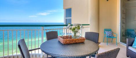 A balcony with a round table, wicker chairs, and a wicker basket with a vase.