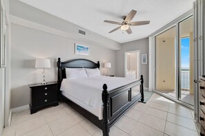 Cozy retreat with a large bed, nightstand, and ceiling fan, offering a view of the outdoor balcony.
