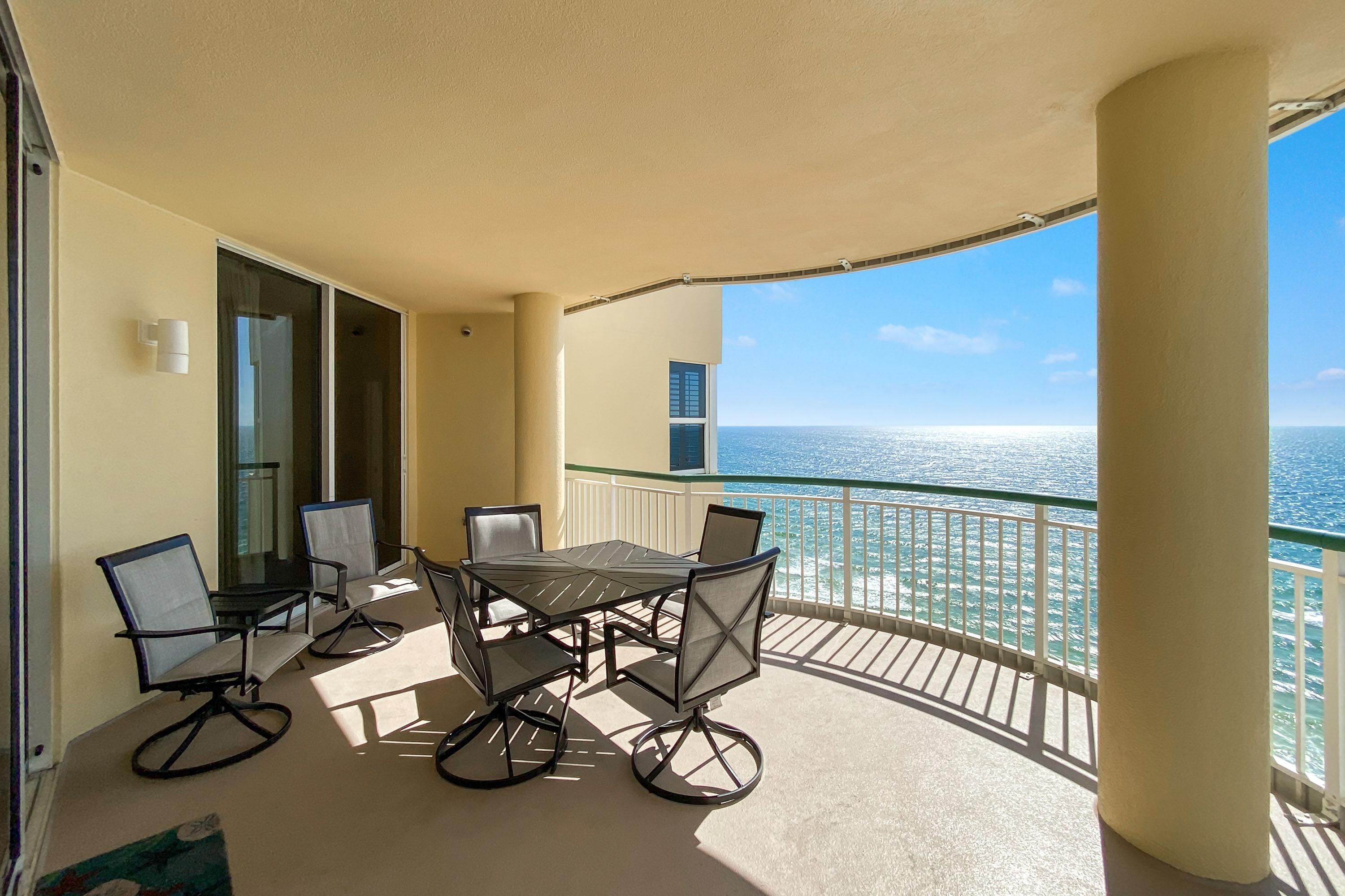 A balcony with a table and chairs, overlooking the sea.