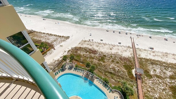 A beach view from a balcony with a pool, beach chairs, and umbrellas.