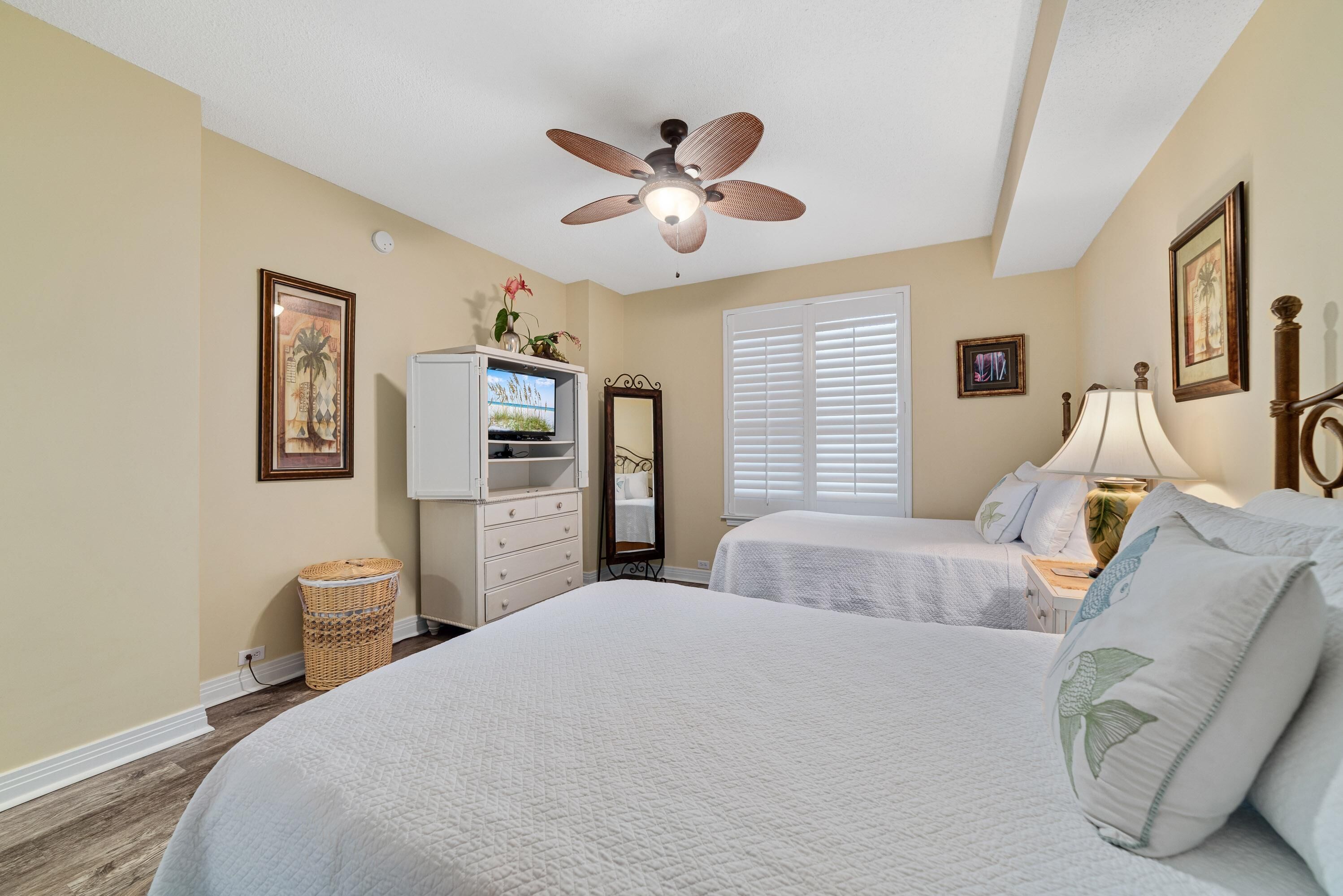 A bedroom with two beds, a ceiling fan, a TV, a dresser, and a window with blinds.