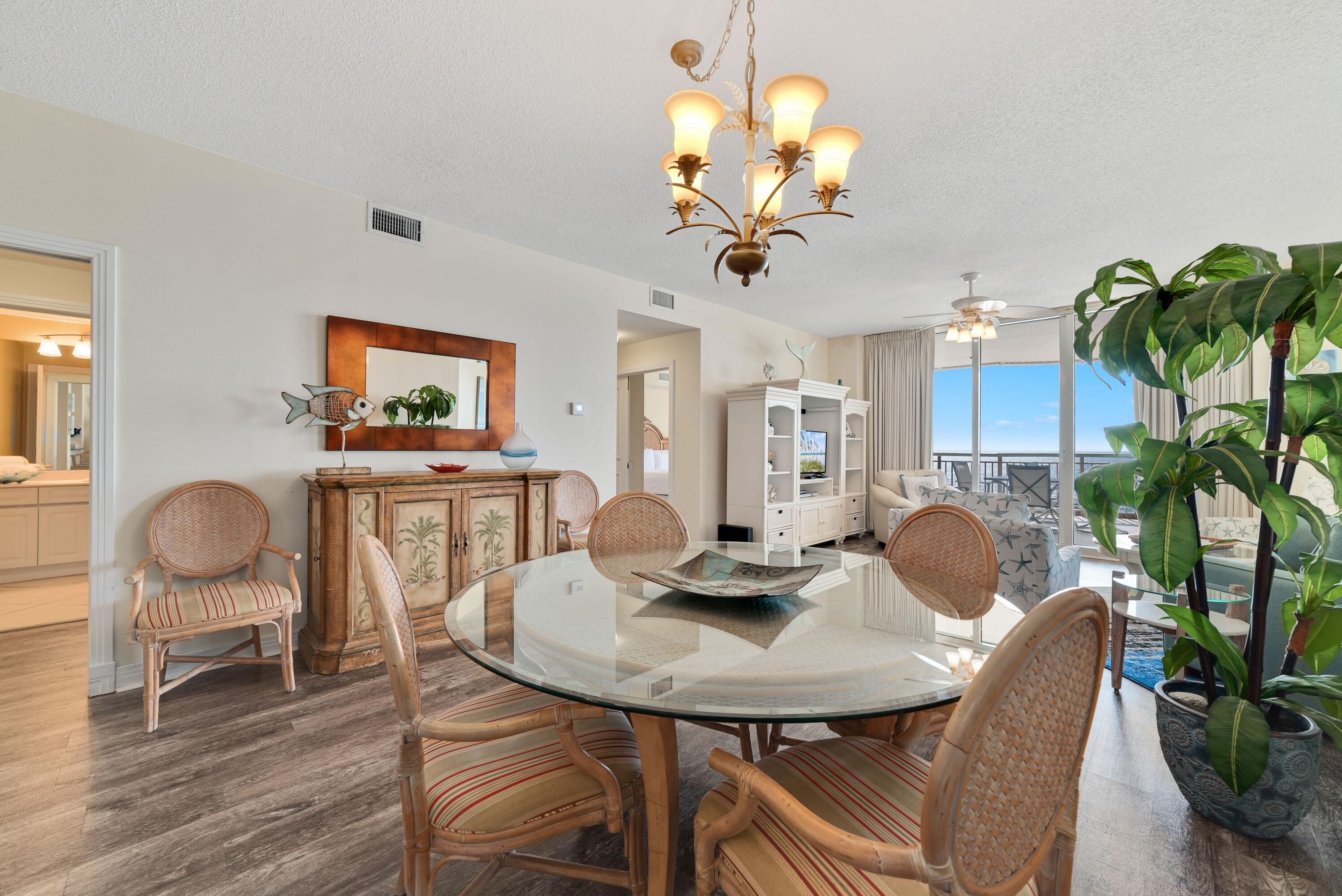 A dining area with a glass table, wicker chairs, a chandelier, and a view of the ocean.